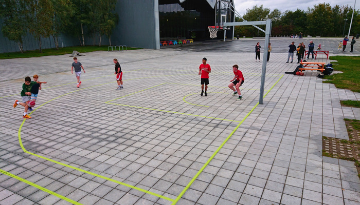 Young people play on an outdoor basketball court near the entrance of the Riverside Museum.