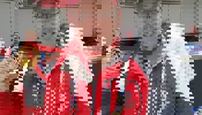 Andrew McVie wearing his red, white and grey Clyde-sider uniform in Glasgow Airport, and he has one of the Glasgow 2014 gold medals around his neck.