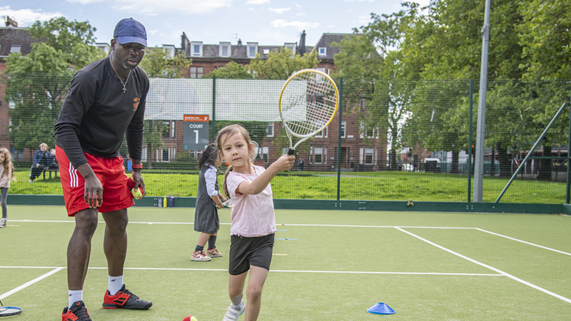 Child playing tennis with coach nearby