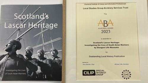 Close up of the cover of a book showing a black and white photo of sailors next to a certificate for Outstanding Local History Publication 