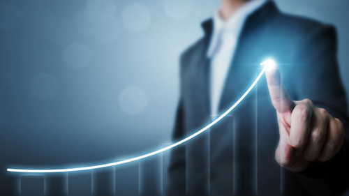 A finger tracing an upward curve on a graph on a screen. In the background is the shape of a figure in business dress.