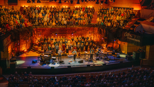 Balcony shot of Karine Polwart performing on stage at Glasgow Royal Concert Hall with musicians and a choir.