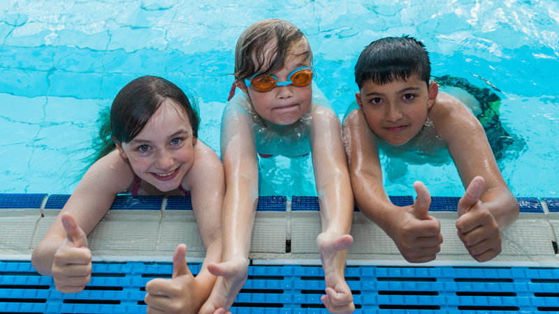 3 kids at edge of swimming pool smiling 