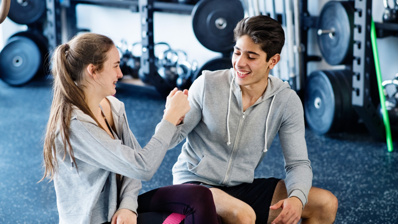 Two teenagers sitting and smiling in the gym