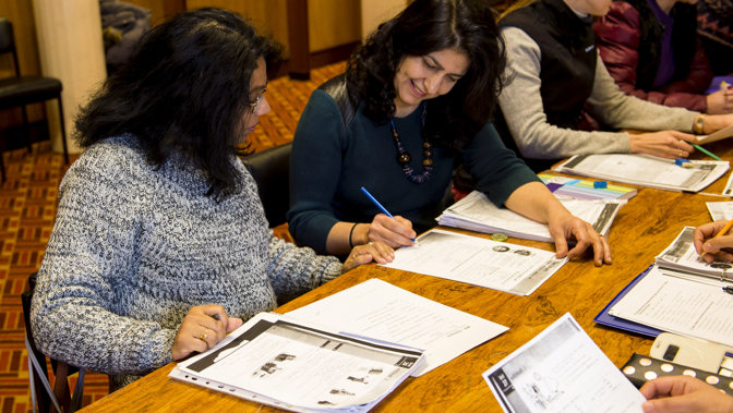 A person is holding a pen while helping another person with some work at a desk in a library.