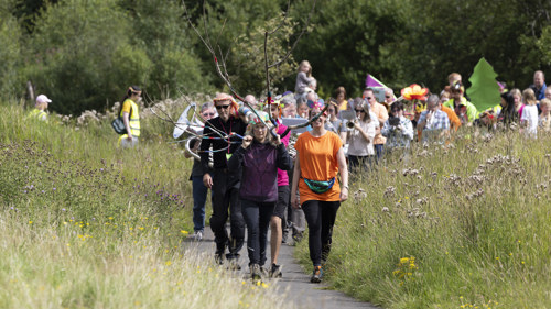 A large group of people walk through a public park in celebratory costume as part of Cowlairs festival