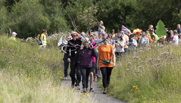 A large group of people walk through a public park in celebratory costume as part of Cowlairs festival