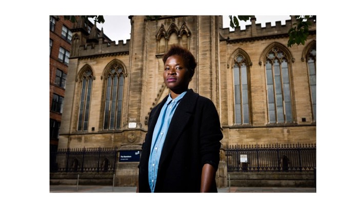 a person standing in front of an older building with tall pointed windows.