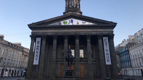 Classical building with columns at the front, decorated with banner advertising Banksy exhibit