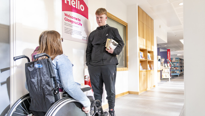 A person in a wheelchair talking to someone standing in a corridor