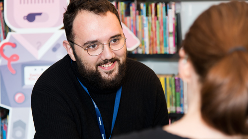A man facing a women, giving advice and smiling in a library setting