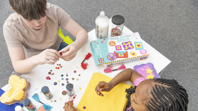 The camera is elevated and looking down at table where two children are creating colourful crafts