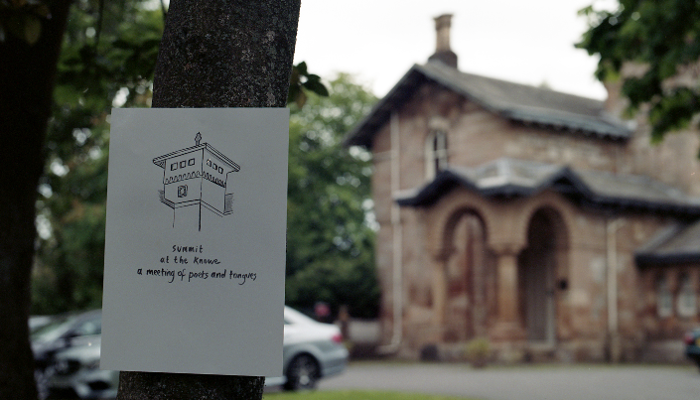 A sign is attached to a tree it reads "summit at the knowe a meeting of poets and tongues".