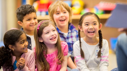South, East Asian and white kids sitting together in a library and smiling.