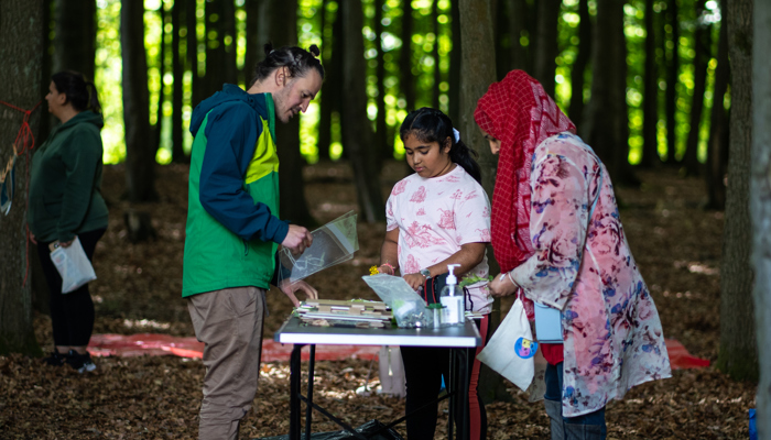 An artist engaged and adult and young teen with books and objects in a wooded area. 