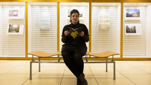 Communities and Libraries Officer Stef sits on a bench in the Mitchell Library in front of a new exhibition. She is reading a pamphlet offering tips on activities to help develop a healthier winter routine and tackle Seasonal Affective Disorder this winter. 