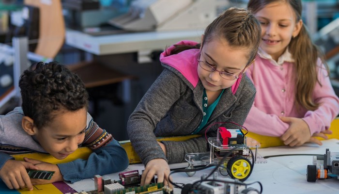 Three children smiling and playing with Lego models as part of a science and technology club.