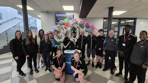 A group of colleagues surrounding balloons to celebrate 30 years. 
