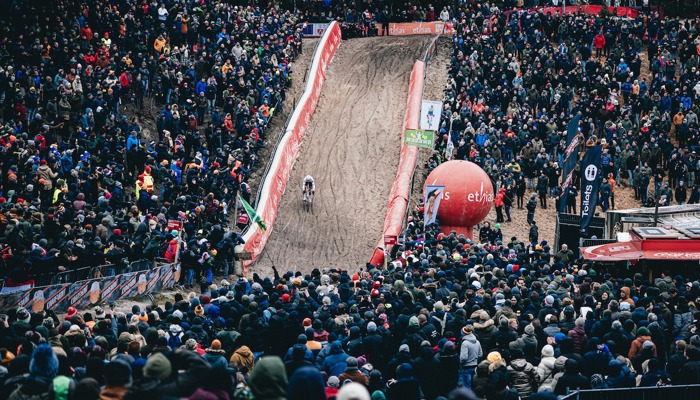 A cyclist races down a cyclo-cross track in front of a large crowd