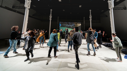 People in multicoloured clothing dance with one another on grey flooring