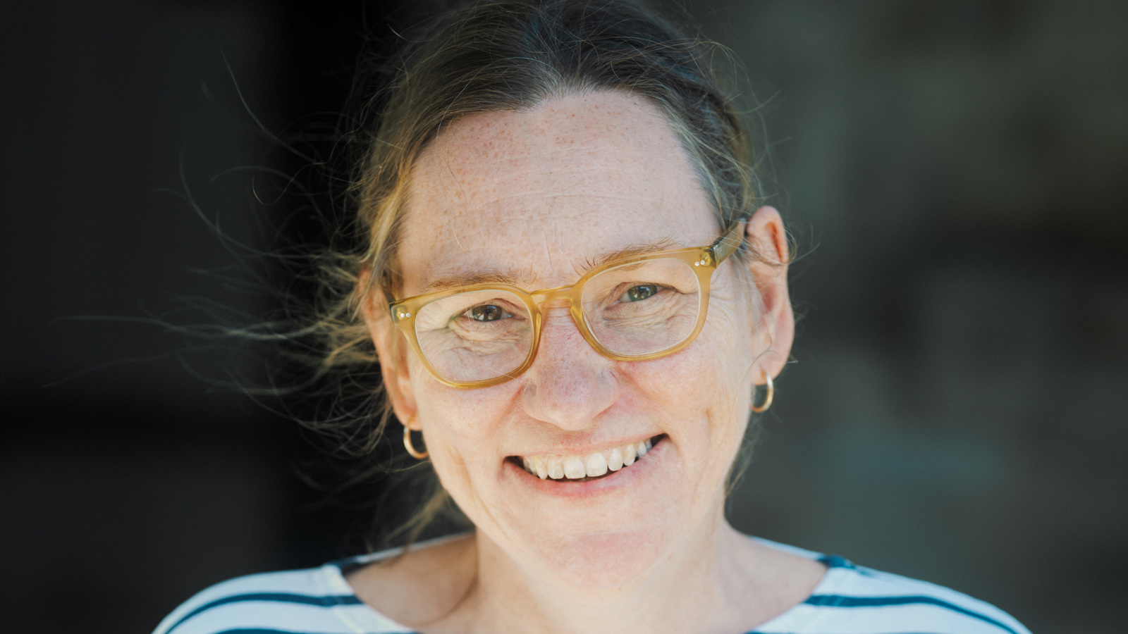 A person wearing glasses and a striped top smiles at the camera