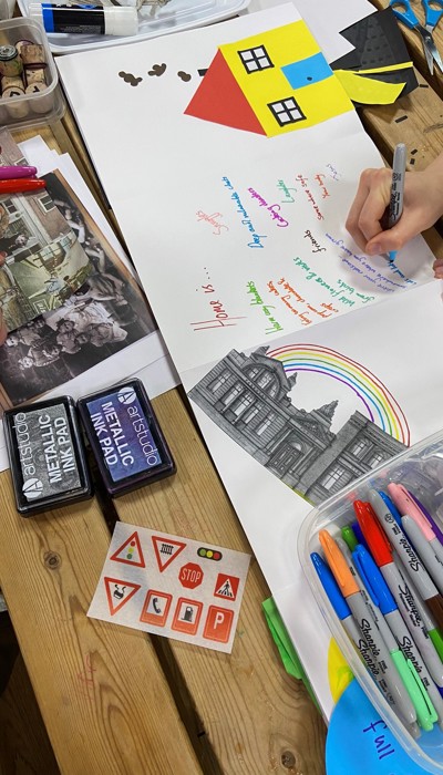 A hand draws on paper they are drawing brightly coloured houses. 