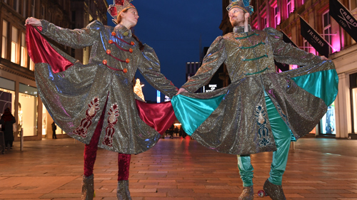 Image of a man and woman dressed as winter swish guards in sparkly costumes with tall hats and roller skates