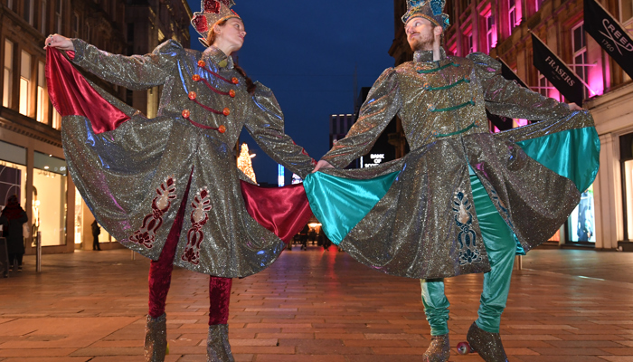 Image of a man and woman dressed as winter swish guards in sparkly costumes with tall hats and roller skates
