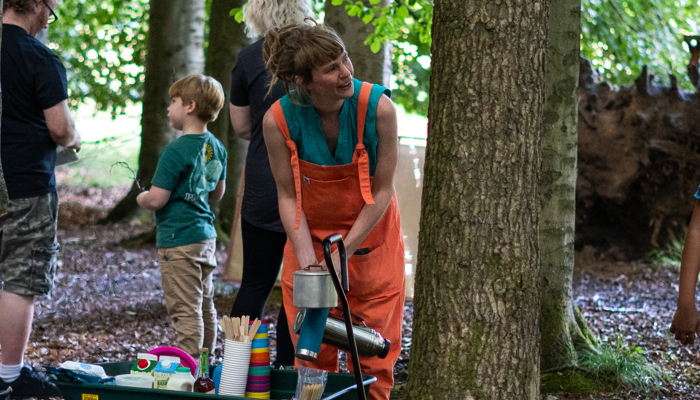 An artist reaches down to get materials out of a wagon, in a wooded area.