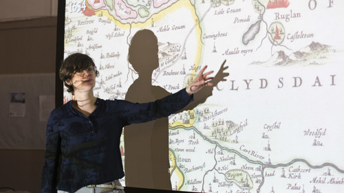 A person stands in front of a historic map which is projected. 