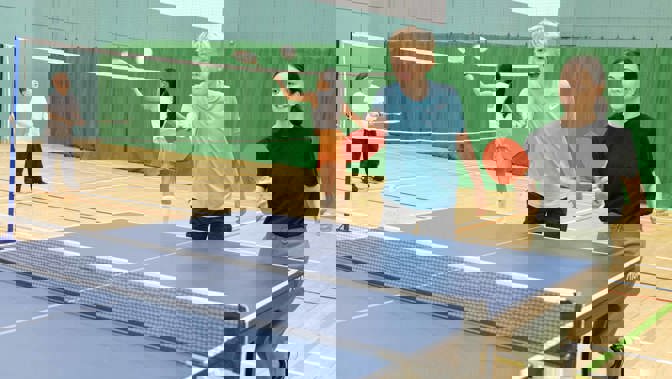 A boy and girl are playing tennis in an indoor court, in the background people are playing pickleball