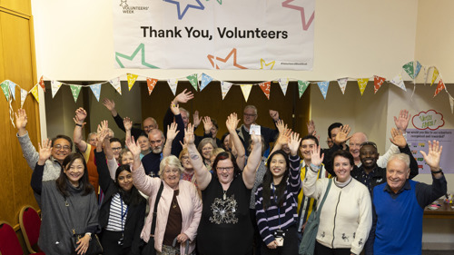 Photo of a large group of people  indoors standing under a sign "thank you volunteers"  looking at the camera 