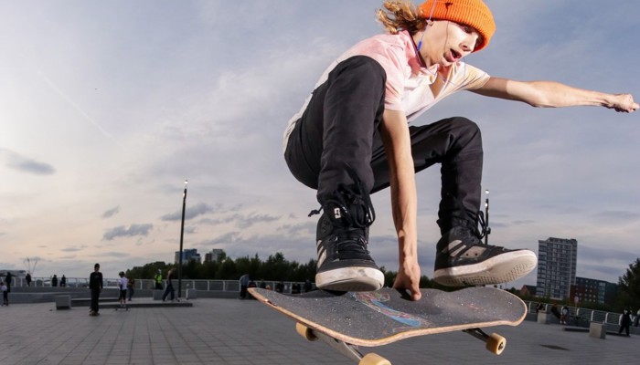 A skateboarder wearing an orange hat, a light top and dark trousers flies through the air mid-stunt