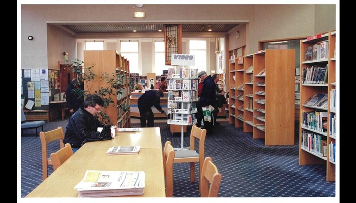 Colour photograph of a library. Desks and bookcases are in the room, and someone is sitting at a desk.