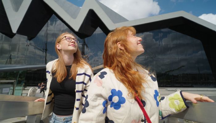 Two visitors take in their surroundings outside a museum with a modern wave-shaped frontage