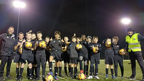 A large group of young football players with their coaches, posing for a photo on a flood lit pitch