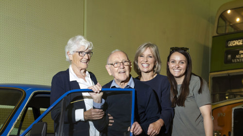 A smiling gentleman, Angus Dougall, who donated his Talbot Avenger Estate stands in front of the blue car with his wife, daughter STV presenter Rona Dougall and granddaughter in Riverside Museum