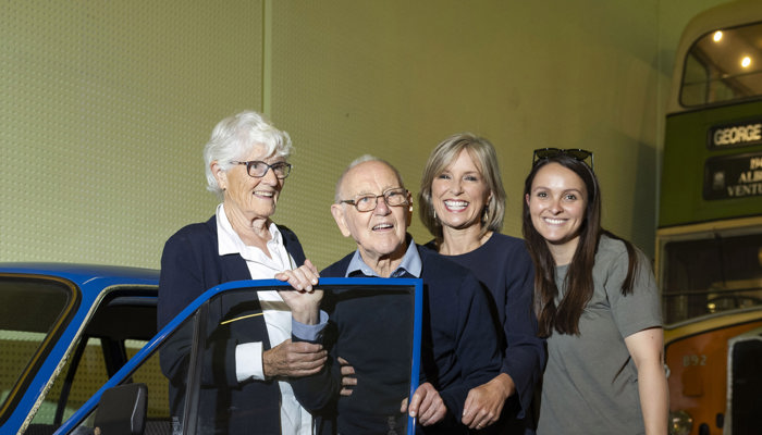 A smiling gentleman, Angus Dougall, who donated his Talbot Avenger Estate stands in front of the blue car with his wife, daughter STV presenter Rona Dougall and granddaughter in Riverside Museum