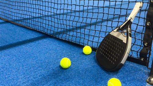A padel racquet and three balls against a net in an indoor padel court