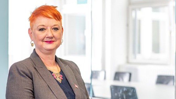Chair of Glasgow Life board, Chair Bailie Annette Christie wearing a grey suit jacket and blue top against a bright window