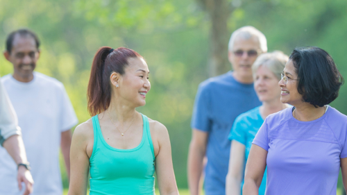 A group of six people walking in a park on a sunny day. They are wearing summer active clothes, smiling and chatting to each other