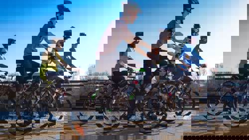 A group of four people cycling along a riverside path in a city centre. They are wearing cycle helmets.