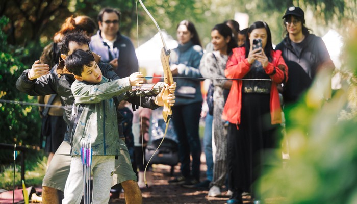 A child tries archery as a crowd watches on in the background