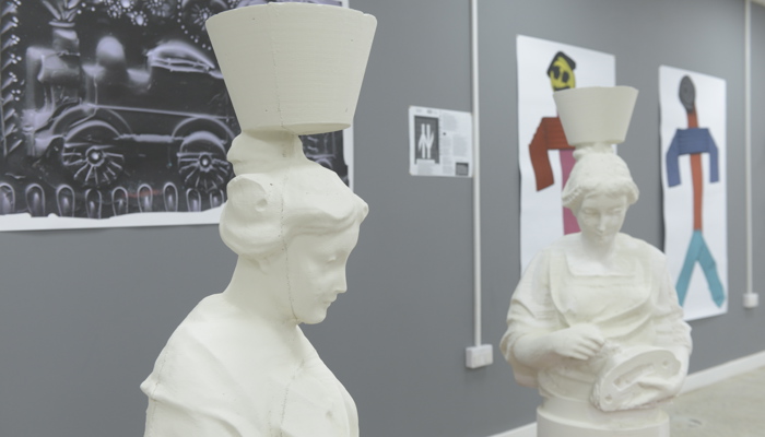 Two statues of "mother Glasgows" are displayed on red pallets. In the background there are painting and prints. 