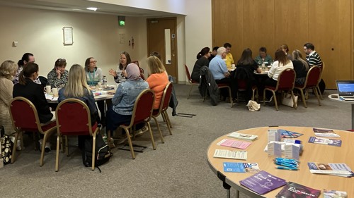 Two groups of ten people sitting around two round tables for group discussion in a meeting room. There are several leaflets displayed on the table next to them.