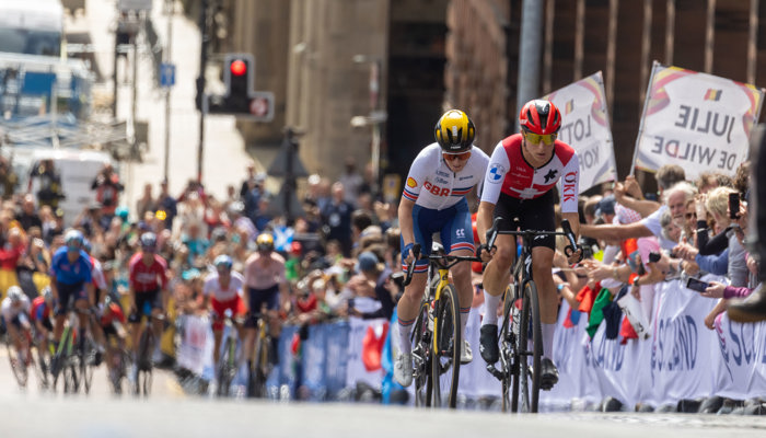 Cyclists racing up the hill on Montrose Street in Glasgow during the 2023 UCI Cycling World Championships in front of cheering crowds of people.