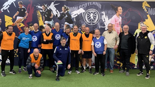 A large group of football players dressed in sports kit posing for a photo at an indoor football pitch