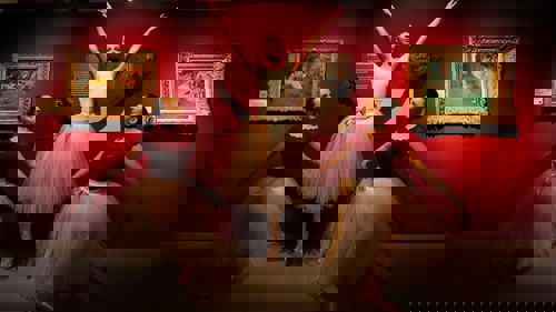 Three ballet dancers holding ballet poses in front of Degas paintings of ballet dancers