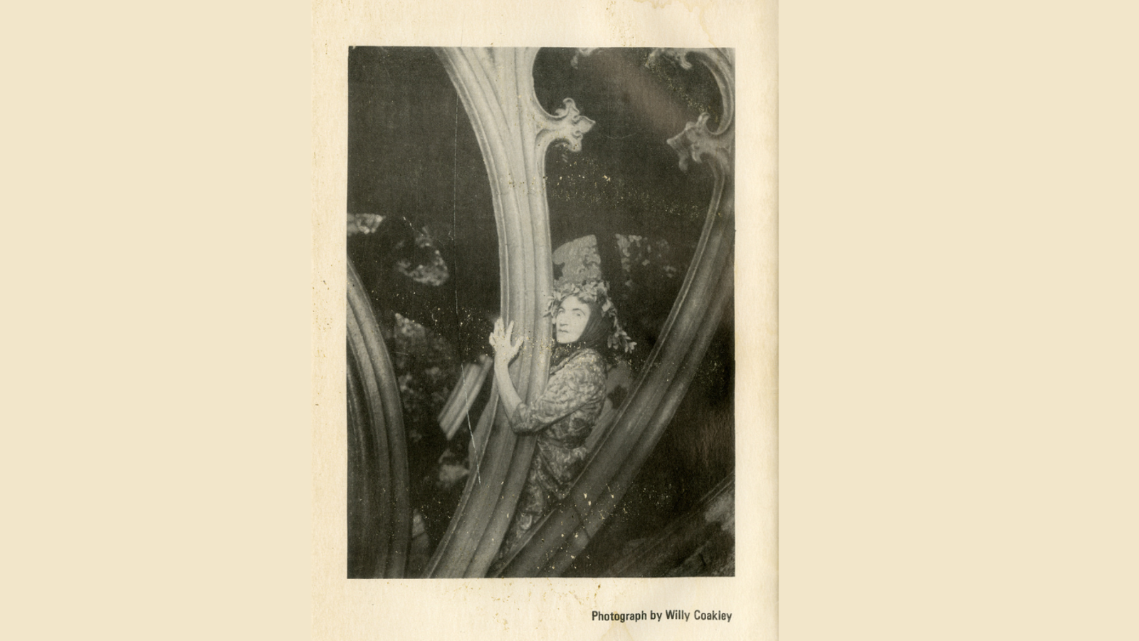 Photograph of a woman wearing a headscarf. She is looking at the camera, sitting on some ornate railings or carvings.