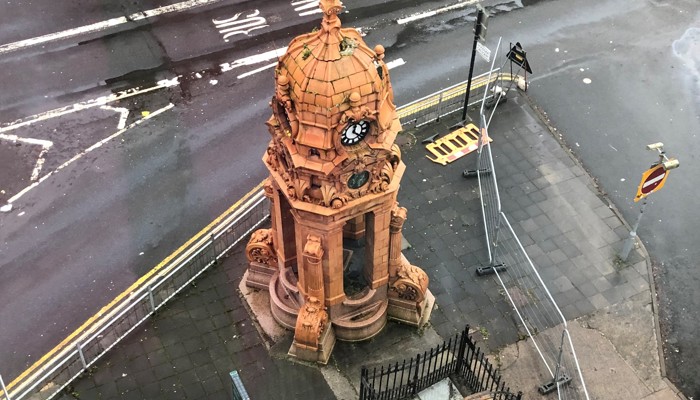 A terracotta fountain with a lean, against a grey street.